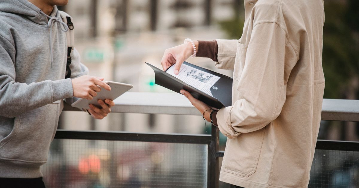 Side view of crop anonymous male students in casual outfits with tablet and folder standing on street and discussing details of research